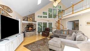 A spacious living room with a fireplace, a large flat-screen TV, a comfortable sofa, and a staircase leading to an upper level.
