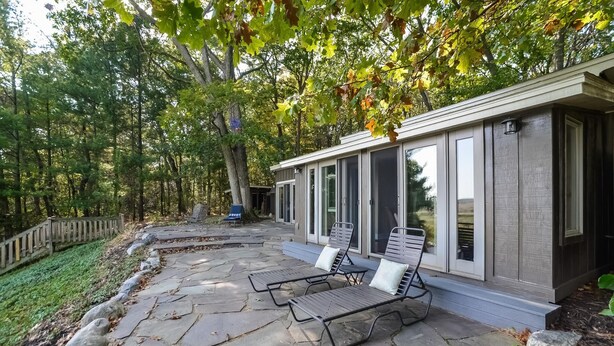 Un patio de piedra con dos sillones y una zona cubierta con puertas correderas de vidrio.