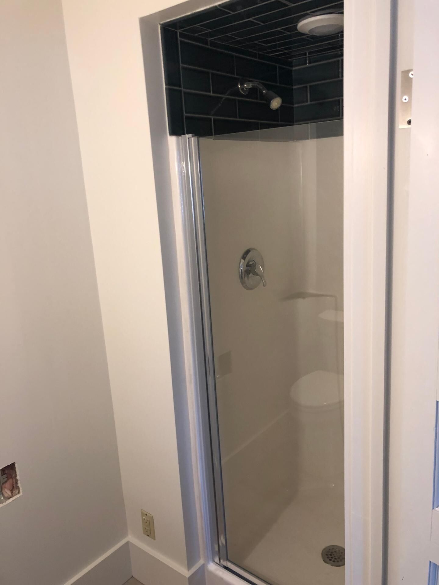 A glass-enclosed shower with a black tiled top, a chrome handle, and a visible drain.