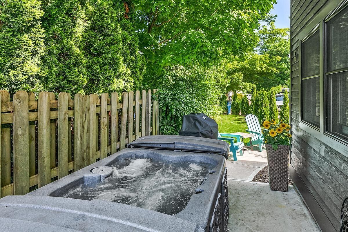 A hot tub in a backyard with a wooden fence, a chair, and a planter with flowers.