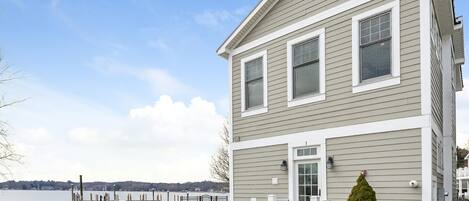 A two-story house with a dock extending into a lake, a small front yard, and a well-maintained lawn.