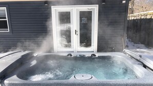 Un bain à remous dont la vapeur s'élève, entouré d'un mur extérieur sombre et doté d'une porte en verre.