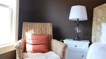 Un dormitorio acogedor con una silla de mimbre, una mesita de noche con lámpara y una cama con cabecera estampada.