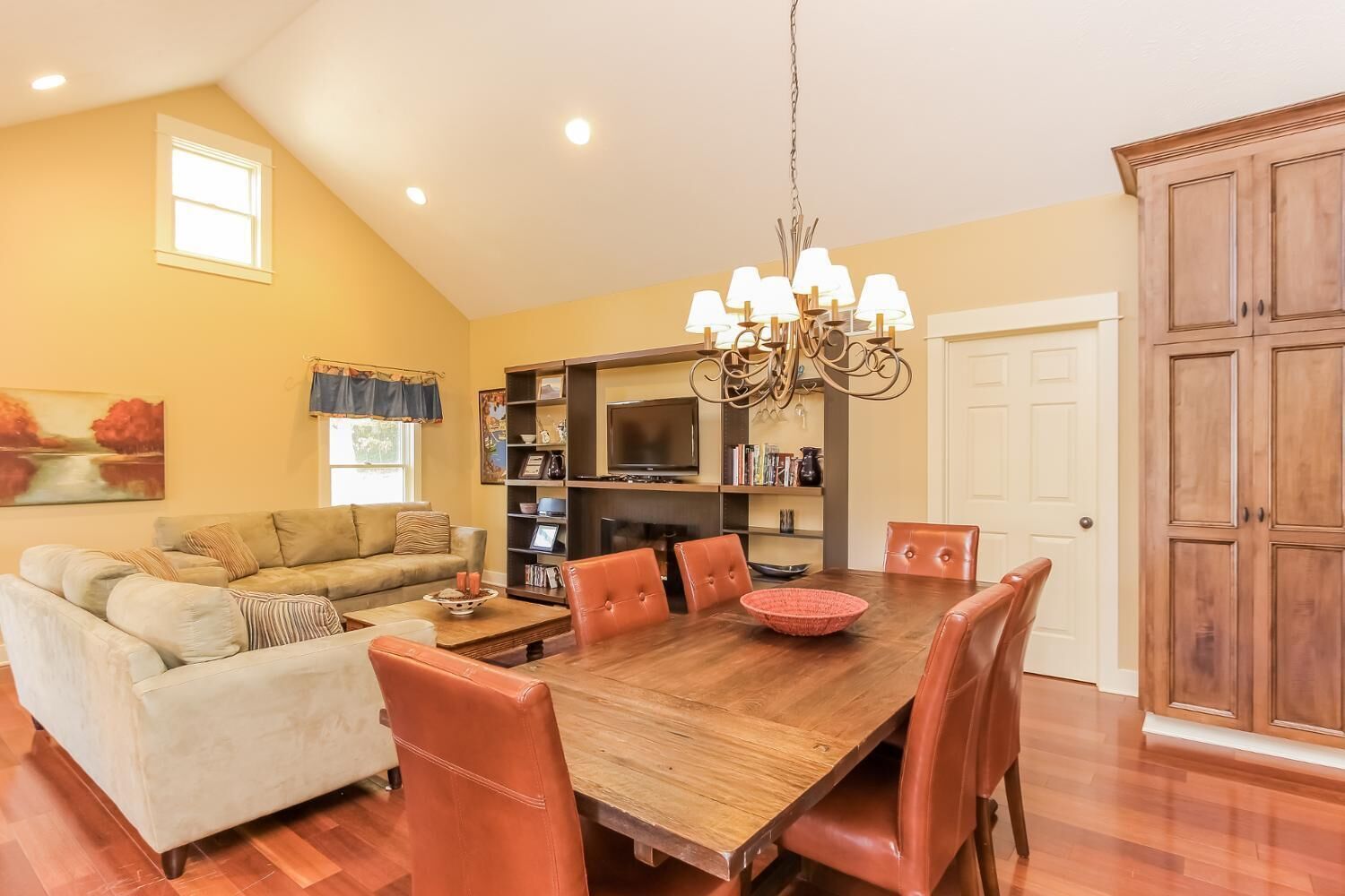 A dining area with a wooden table and chairs, a chandelier, and a bookshelf with various items.