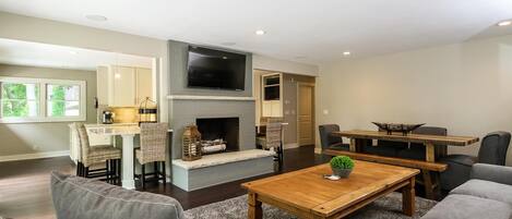 A living room with a fireplace, a TV mounted above it, and a dining area with a table and chairs.