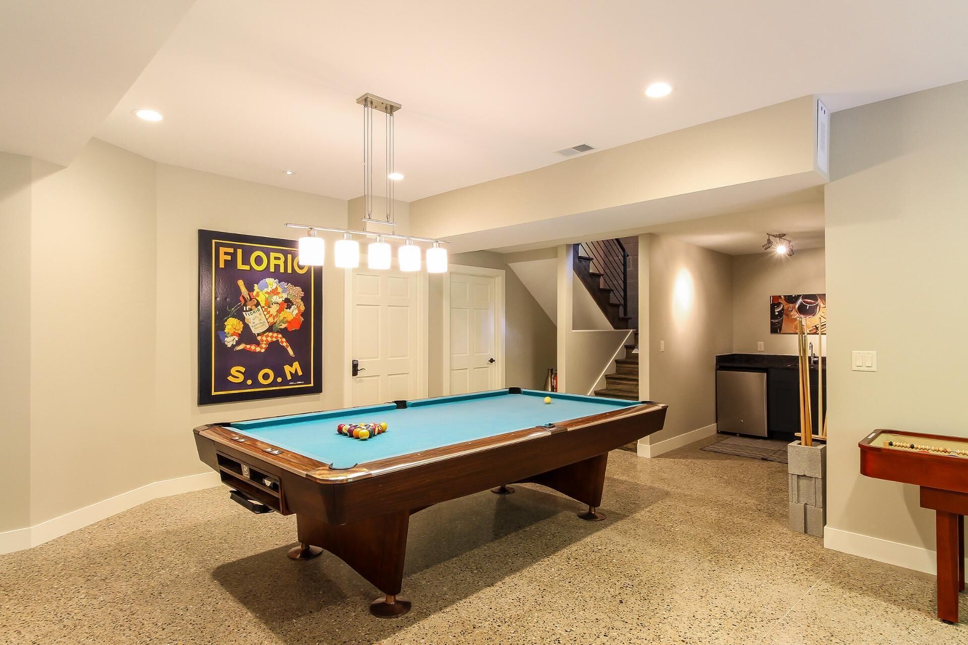 A pool table in a room with a staircase, a door, and a poster on the wall.