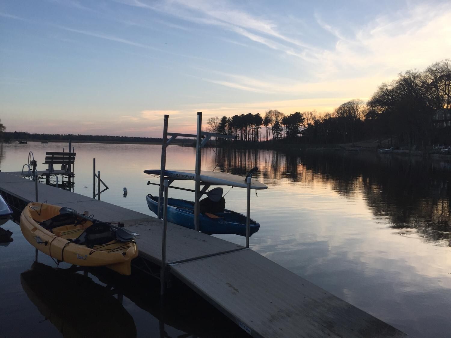 Un lac paisible où des bateaux sont amarrés à un quai, le tout entouré d’arbres.