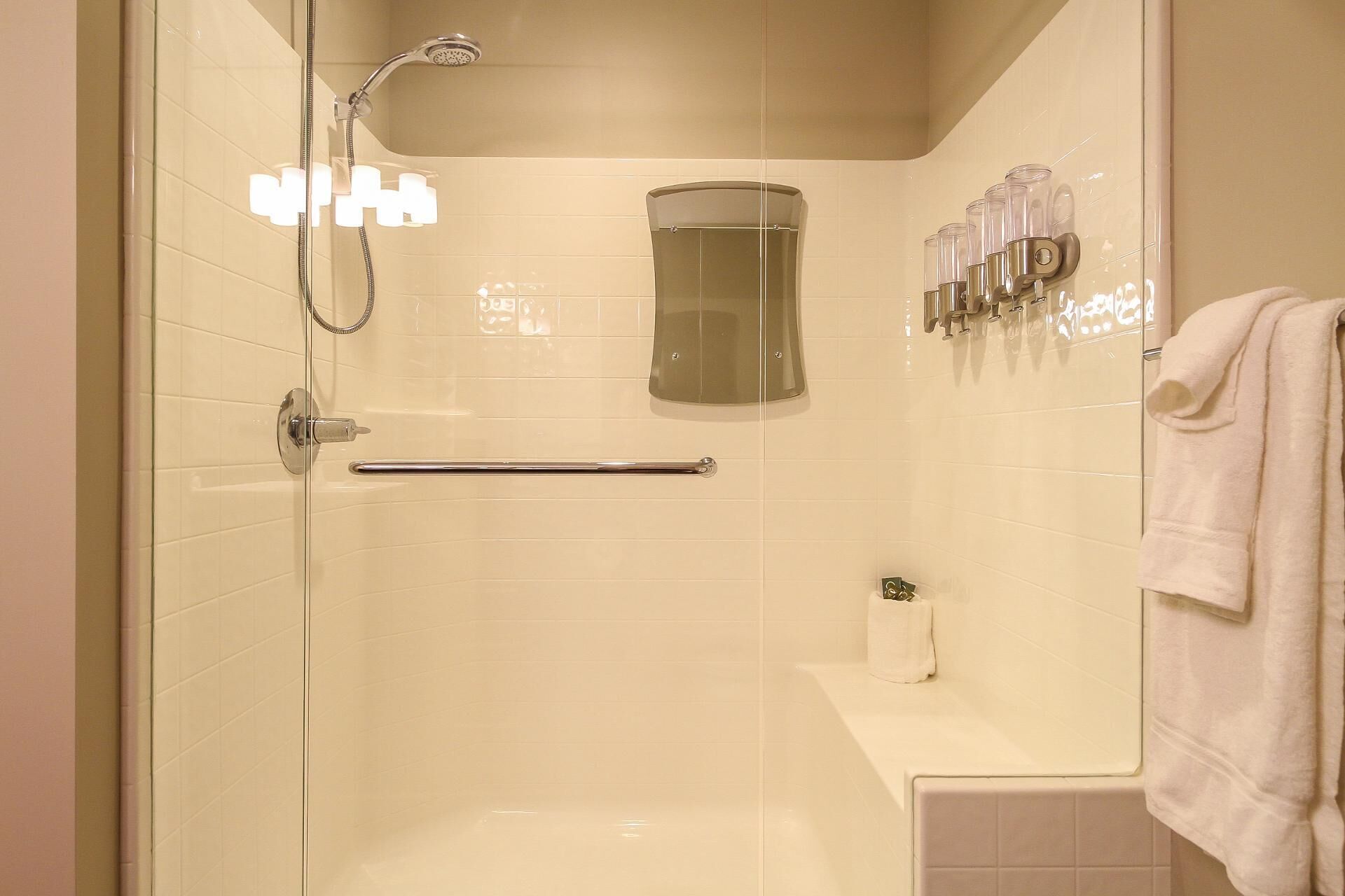 A modern bathroom with a glass-enclosed shower, a handrail, a toilet paper holder, and a towel rack.