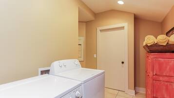 A laundry room with a front-loading washer and dryer, a wooden cabinet with folded towels, and a door leading to another room.