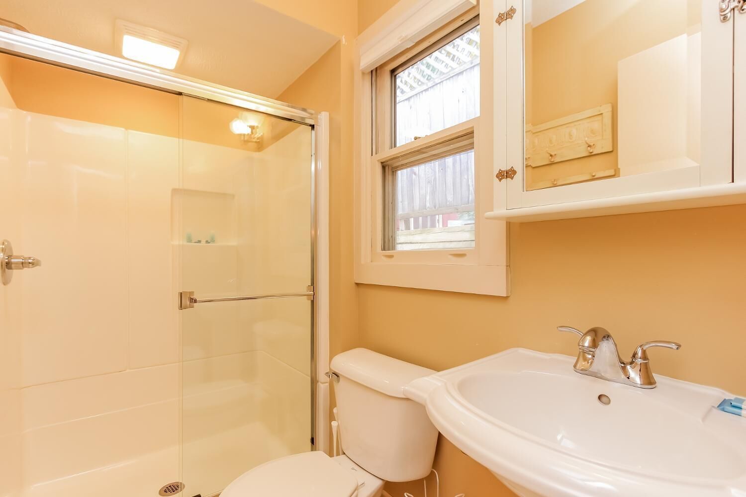A bathroom with a glass shower enclosure, a toilet, and a sink with a window above the mirror.