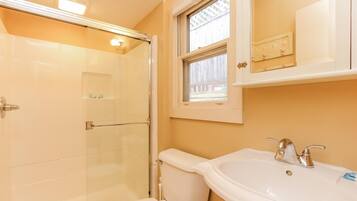 A bathroom with a glass shower enclosure, a toilet, and a sink with a window above the mirror.
