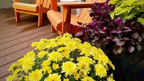 A wooden deck with two orange Adirondack chairs and a large planter with yellow flowers.