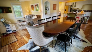 A spacious dining area with a wooden table and chairs, a cowhide rug, and a kitchen in the background.