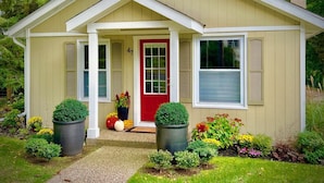 A single-story house with a red door, beige siding, and a small porch.