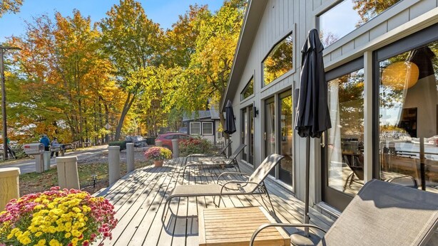 A modern building with a deck featuring outdoor seating and a garden with colorful flowers. - How you Dune (Saugatuck)