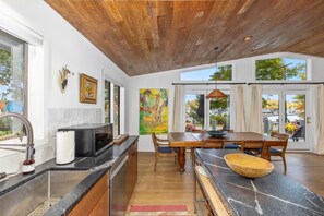 A modern kitchen with a wooden ceiling, large windows, and a dining area with a table and chairs. - How you Dune (Saugatuck)
