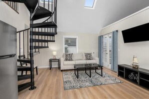 A modern living room with a black spiral staircase, a sofa set, a coffee table, and a TV mounted on the wall. - Riverview Loft (Saugatuck)
