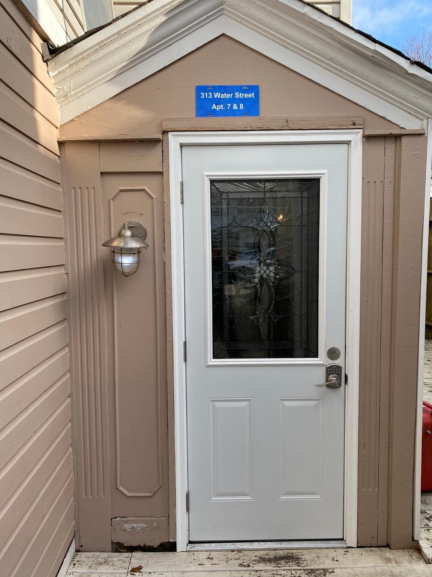 A beige building with a white door, a blue sign above it, and a small light fixture to the left.