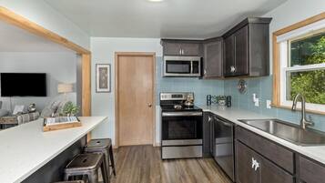 A modern kitchen with dark cabinets, a stainless steel oven, a microwave, and a large window providing a view of greenery.