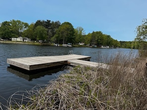 Un muelle de madera se adentra en un lago tranquilo, rodeado de árboles frondosos y un cielo despejado.