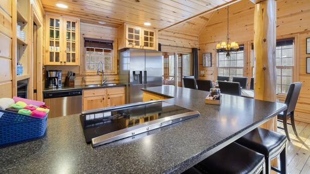 A modern kitchen with wooden cabinetry, a stainless steel refrigerator, and a large island with a built-in stovetop.