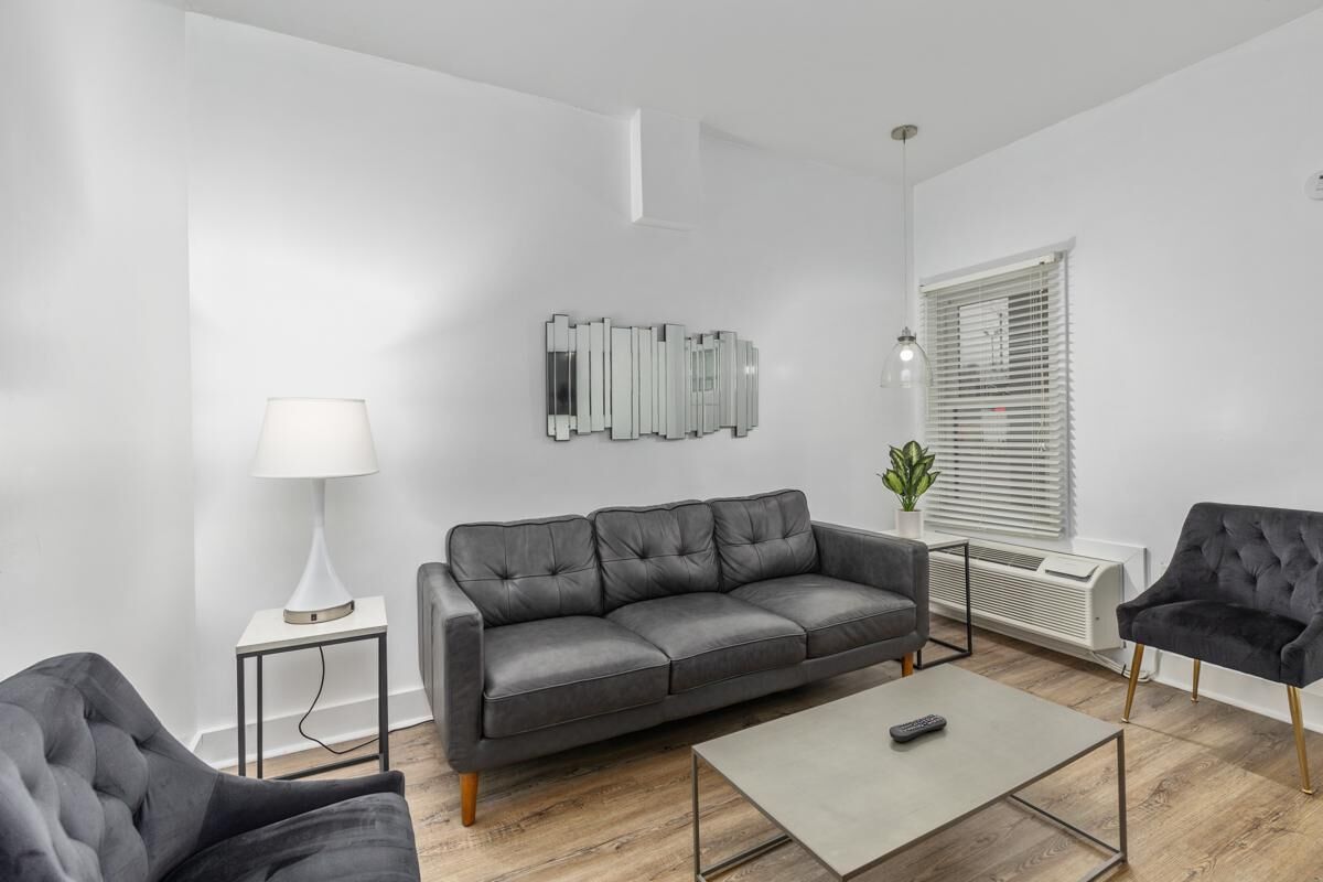 Een moderne woonkamer met een grijze leren bank, een kleine bijzettafel met een lamp, een salontafel en een zwarte fauteuil.