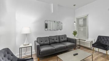 Een moderne woonkamer met een grijze leren bank, een kleine bijzettafel met een lamp, een salontafel en een zwarte fauteuil.