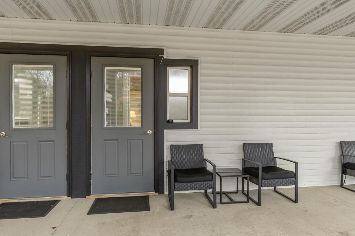 Un porche abrité avec deux portes de couleur gris foncé, une petite table et trois chaises en osier.
