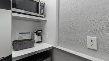 A kitchenette with a microwave, coffee maker, and a basket on the counter.