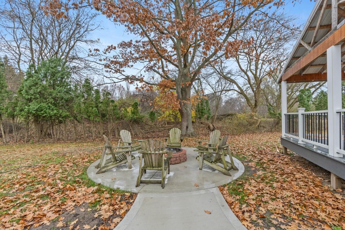 A circular outdoor seating area with Adirondack chairs and a fire pit, surrounded by a concrete path and a wooden deck.