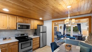A modern kitchen with wooden cabinets, stainless steel appliances, and a dining area with a blue sofa and table. - "cozy Cottages" Green Cottage Hot Tub-town! (Saugatuck)