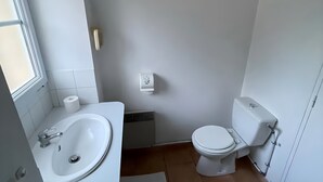 Un baño pequeño y limpio con un lavabo blanco, inodoro y un dispensador de papel higiénico en la pared.