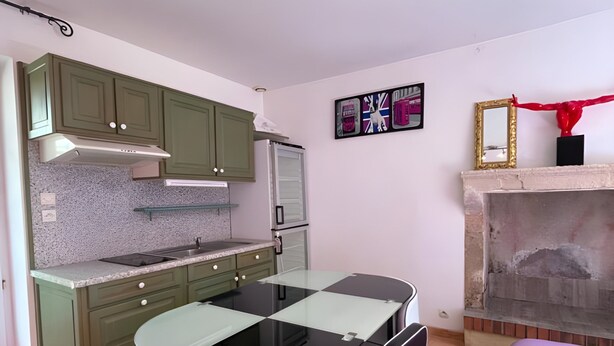 Cocina compacta con armarios verdes, una mesa de comedor negra y dos sillas. Incluye un microondas, una estufa a gas y un ventanal pequeño.