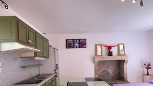 Una cocina compacta con armarios verdes, una estufa moderna y un comedor con mesa de vidrio y dos sillas.