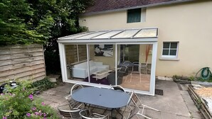 Un invernadero con puerta de cristal, una mesa de comedor y sillas en un jardín.