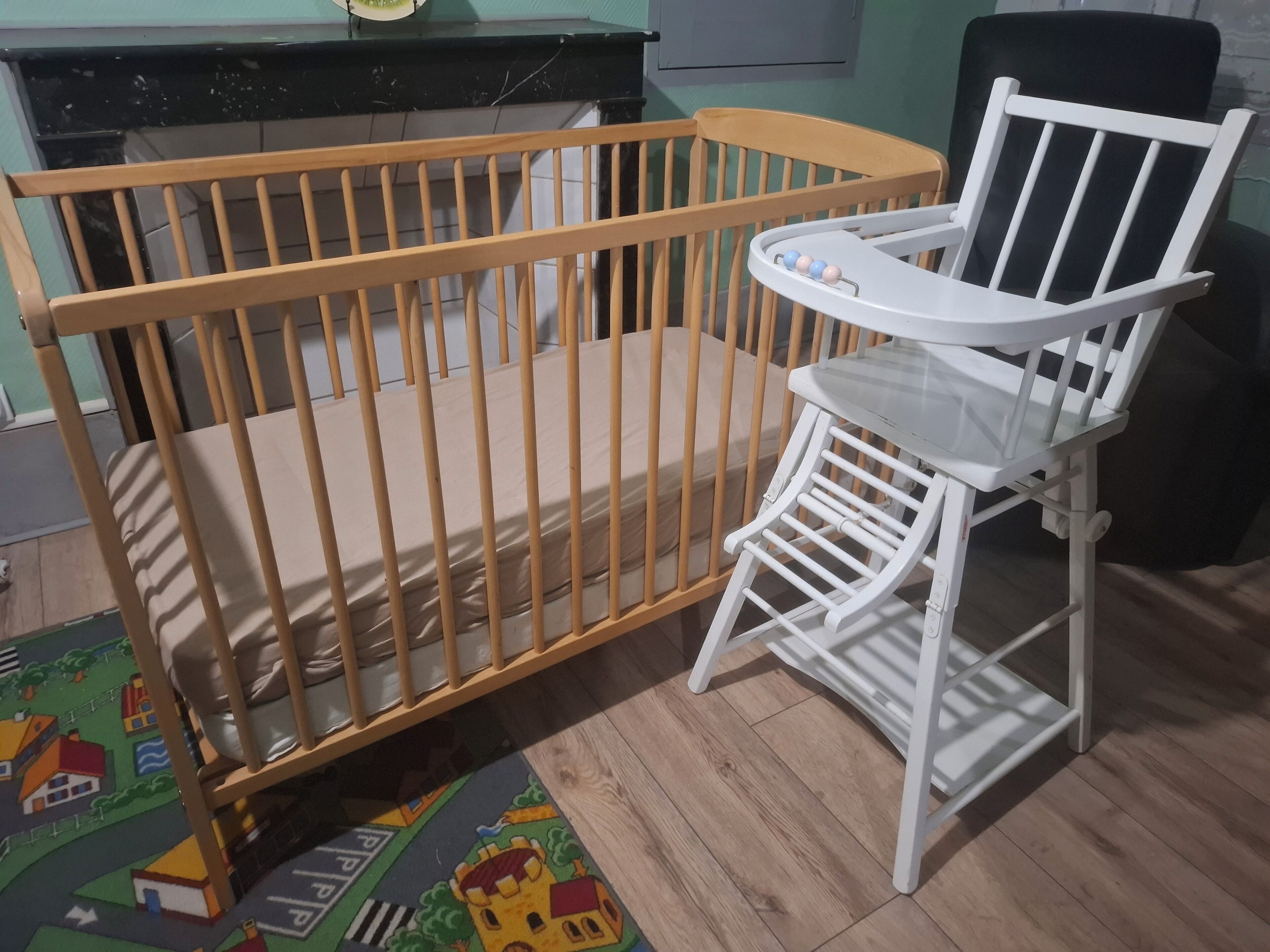 Ein hölzernes Kinderbett mit einem weißen Hochstuhl daneben.