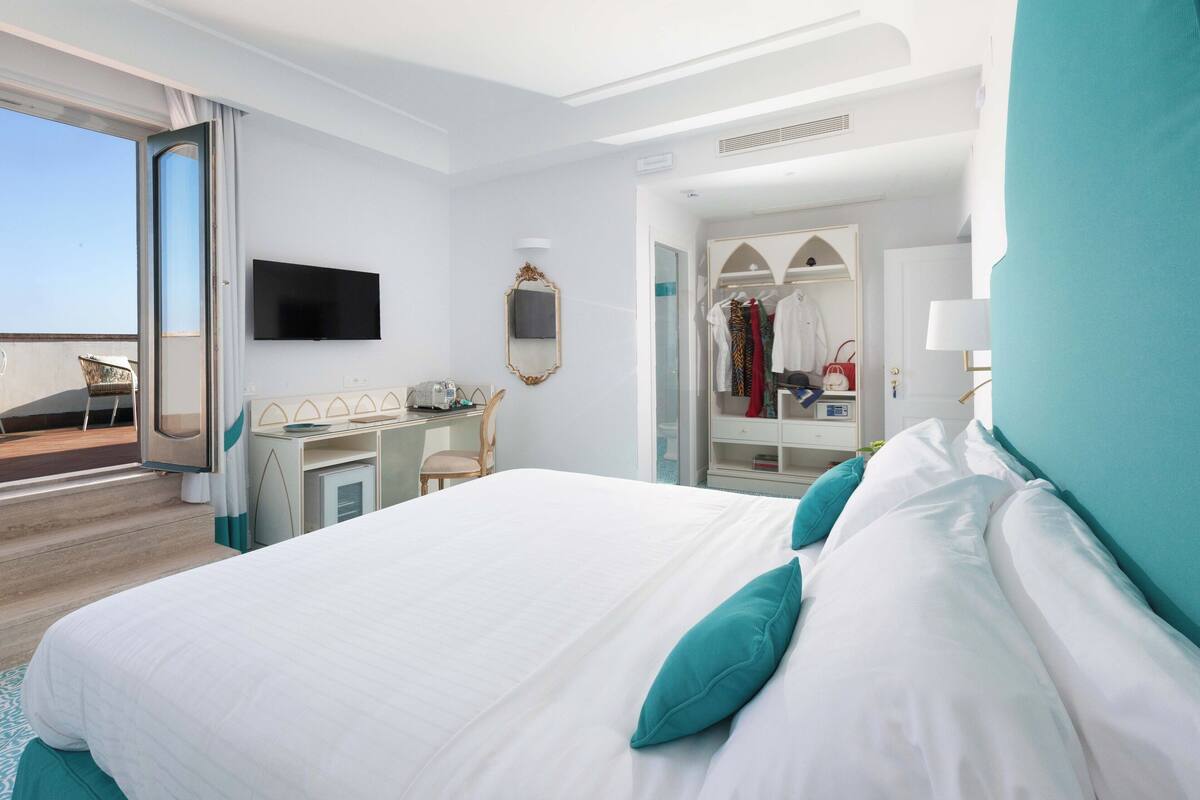 A hotel room with a bed, a desk, a TV, a wardrobe, and a balcony.