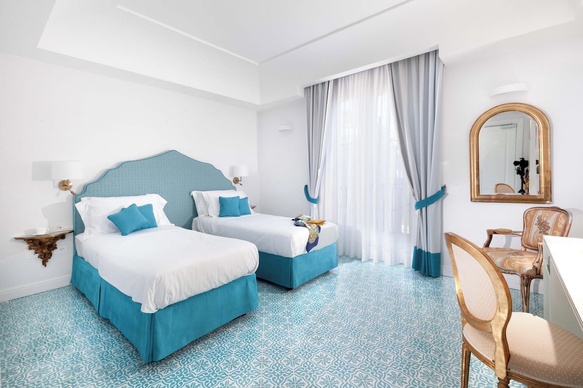 A hotel room with two beds, a desk, a chair, a mirror, and a patterned floor.