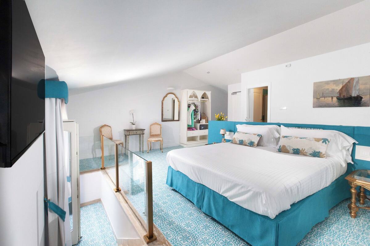 A bedroom with a large bed, a wardrobe, a mirror, and a painting on the wall.