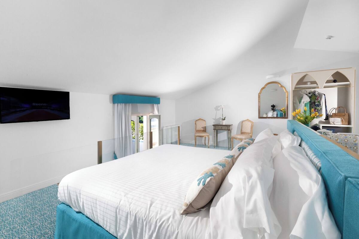 A hotel room with a large bed, a desk, a chair, a mirror, and a television.