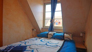A bedroom with a bed, pillows, a window, and a view of a house outside. - Einladende Ferienwohnung im Zentrum von Robel (Röbel/Müritz)
