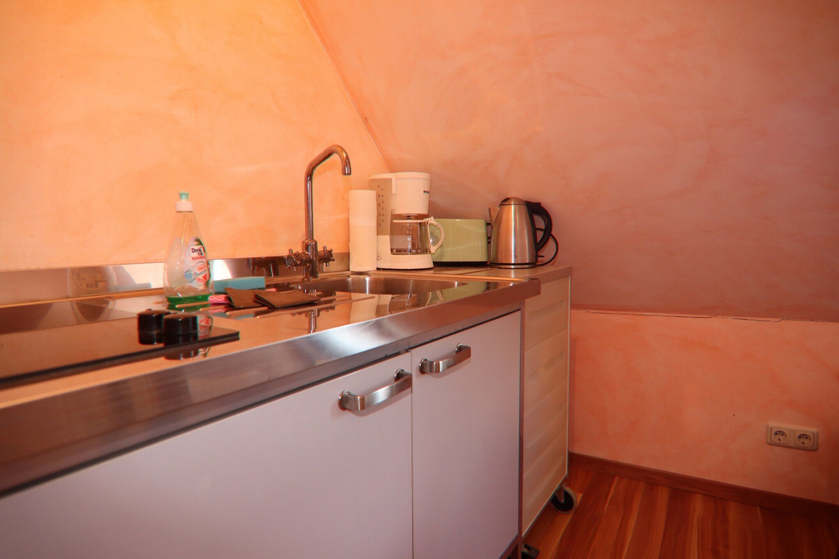 A kitchenette with a sink, faucet, coffee maker, and a bottle of dish soap.