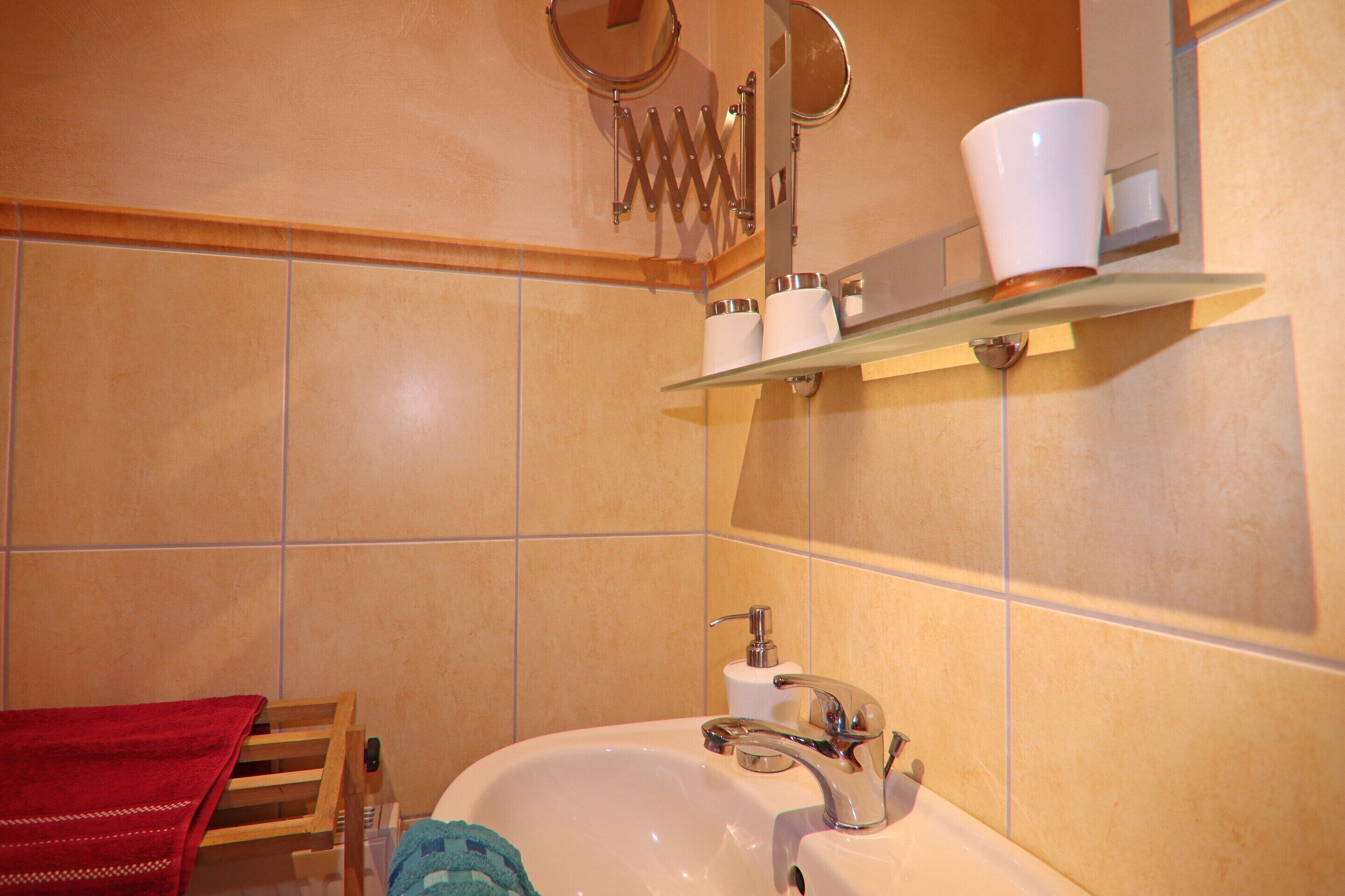 Un baño con lavamanos, espejo y toallero.