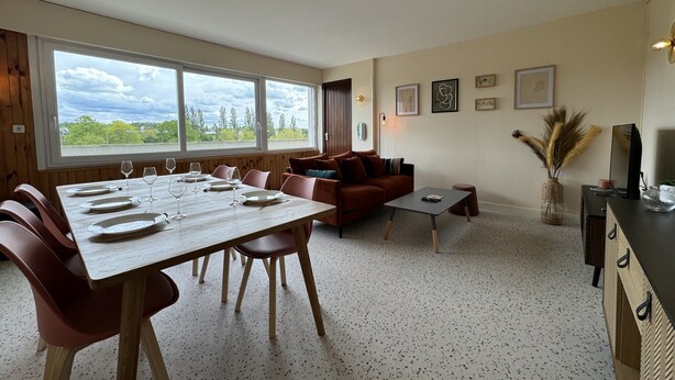 A dining area with a wooden table set for six, a brown sofa, and a small coffee table. - Apartment in Le Mans Near 24H Circuit (Le Mans)