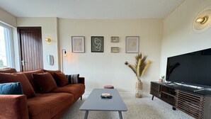 A modern living room with a brown sofa, a coffee table, a TV, and framed artwork on the wall. - Apartment in Le Mans Near 24H Circuit (Le Mans)