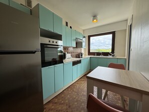 A compact kitchen with teal cabinets, a built-in oven, and a window with a view. - Apartment in Le Mans Near 24H Circuit (Le Mans)