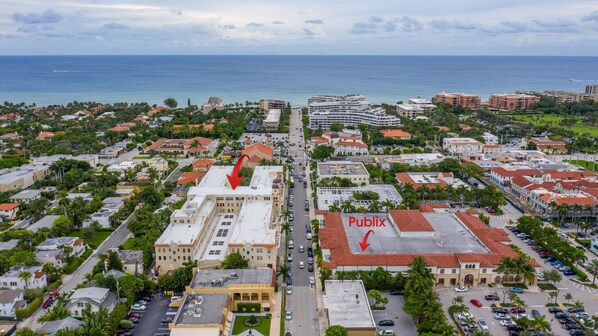 Vista aérea de un pueblo costero con un hotel destacado llamado 'Pueblix', que cuenta con un amplio estacionamiento y una calle principal.