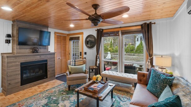 Un salón acogedor con chimenea, televisor, sofá y un ventanal con cortinas.