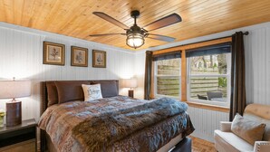Un dormitorio con techo de madera, cama con manta de piel, una silla y ventana con vistas al exterior.