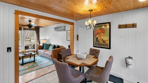 Una sala de estar acogedora con techo de madera, un comedor con mesa y sillas, y un cartel grande en la pared.
